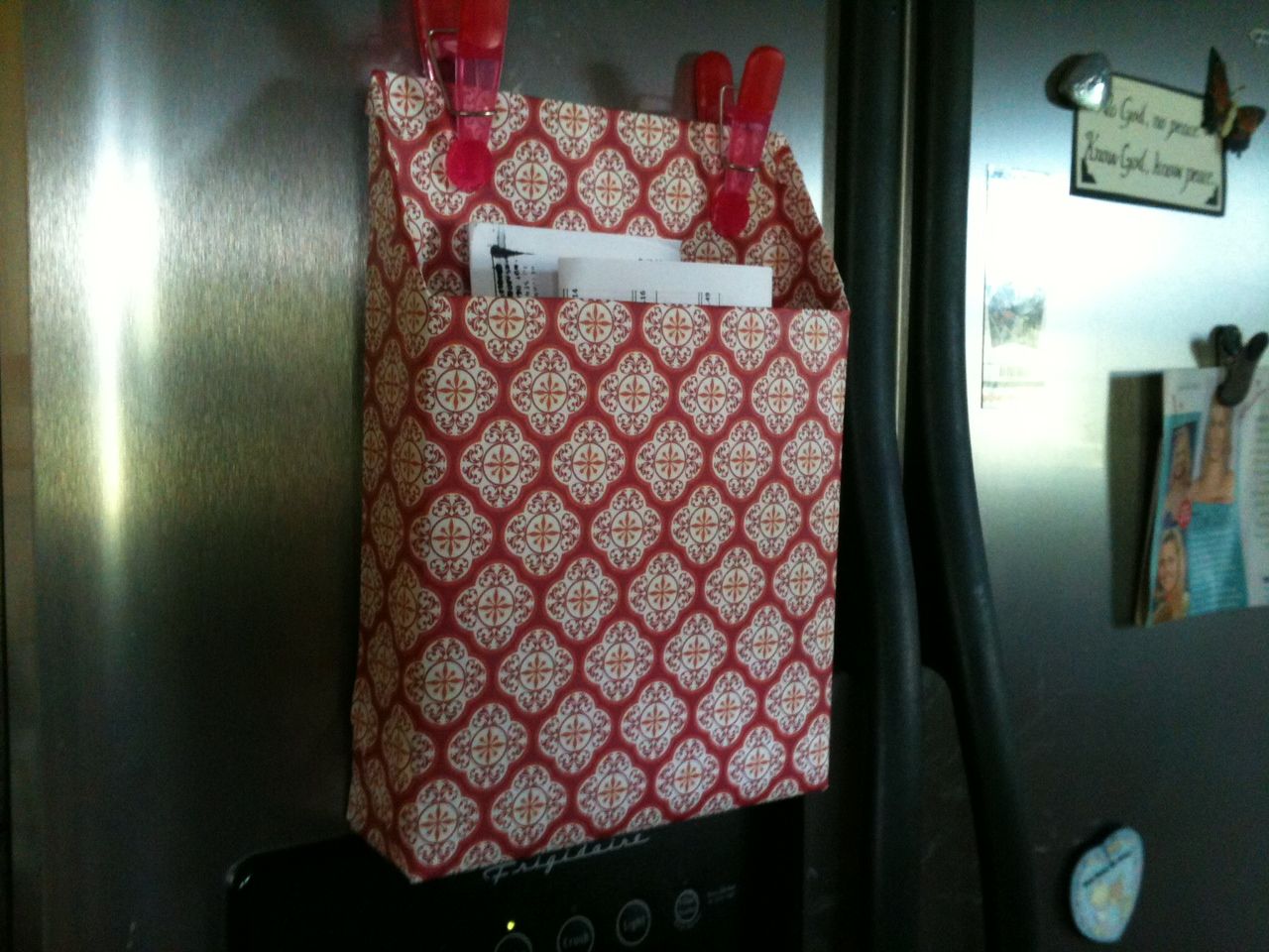 Cereal box covered in scrapbook paper with magnets on the side of the fridge. Gr