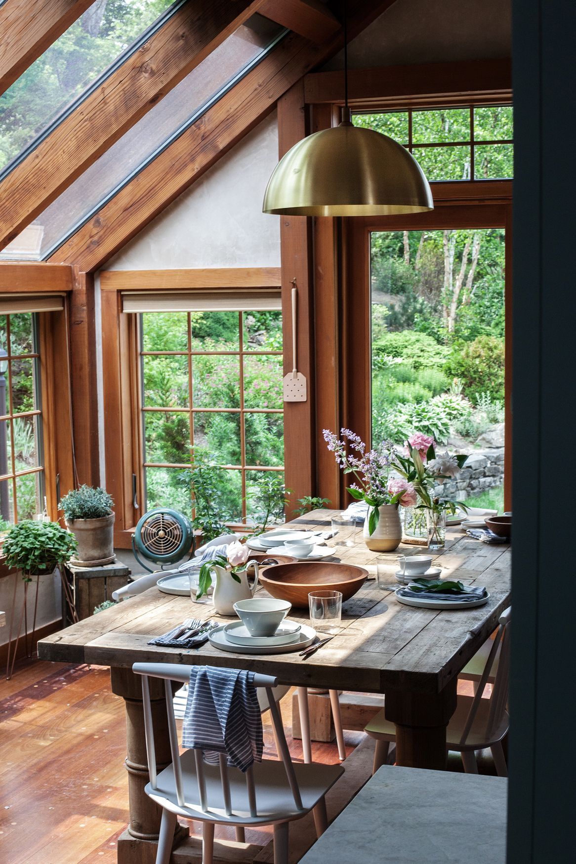 A brass pendant light over the farm table adds a modern touch to this cottage-style sun room. Photo by