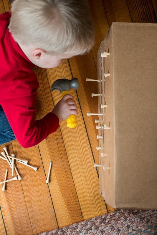 Pounding tees into a cardboard box – great idea for fine motor skills for toddlers