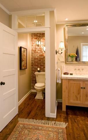 Toilet closet with wood floors, brick wall and transom window