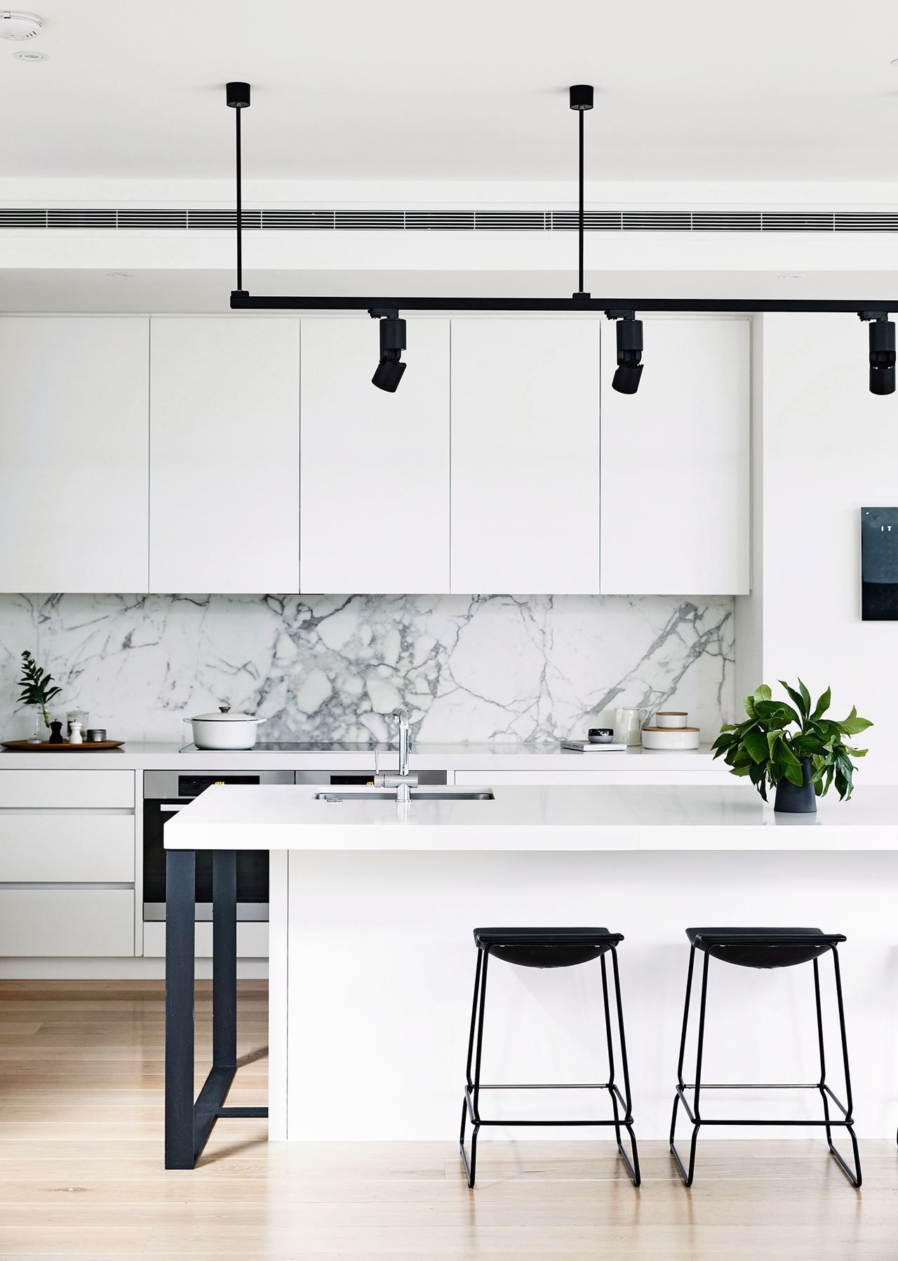 Black and white monochrome kitchen: handleless white cabinets and benchtops, grey marble splashback, black bar stools, black