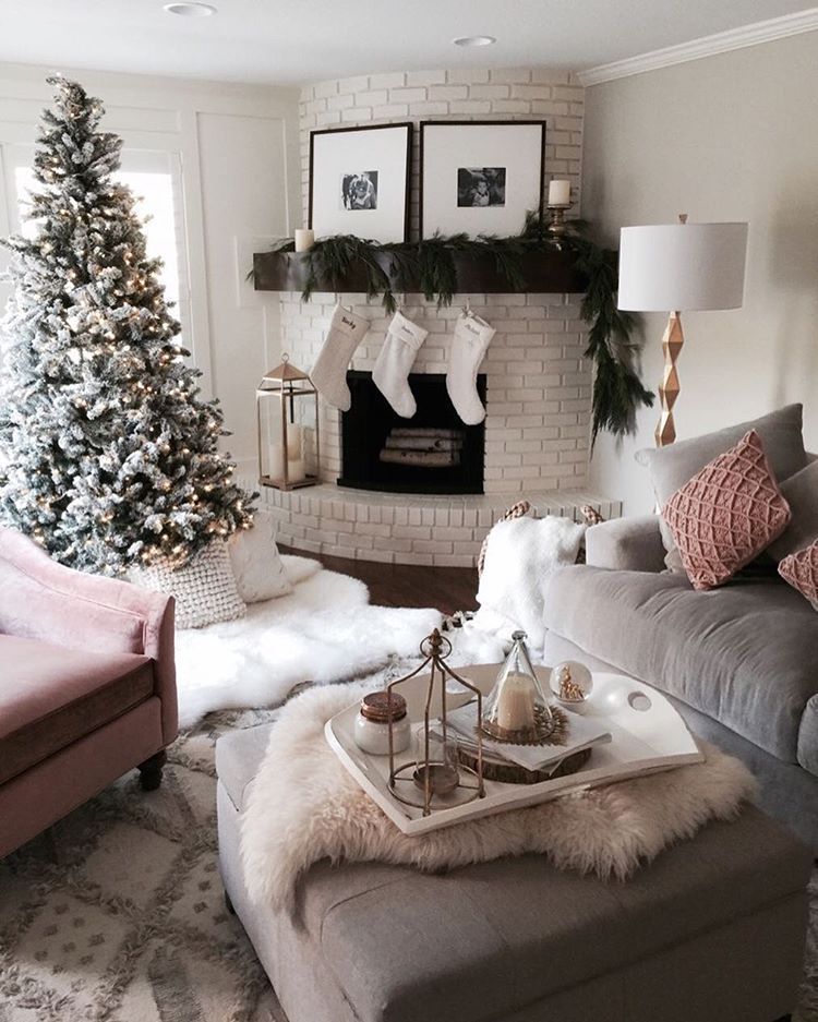 Christmas tree, white brick fireplace, velvet grey couch, velvet pink loveseat, upholstered square ottoman. White neutrals