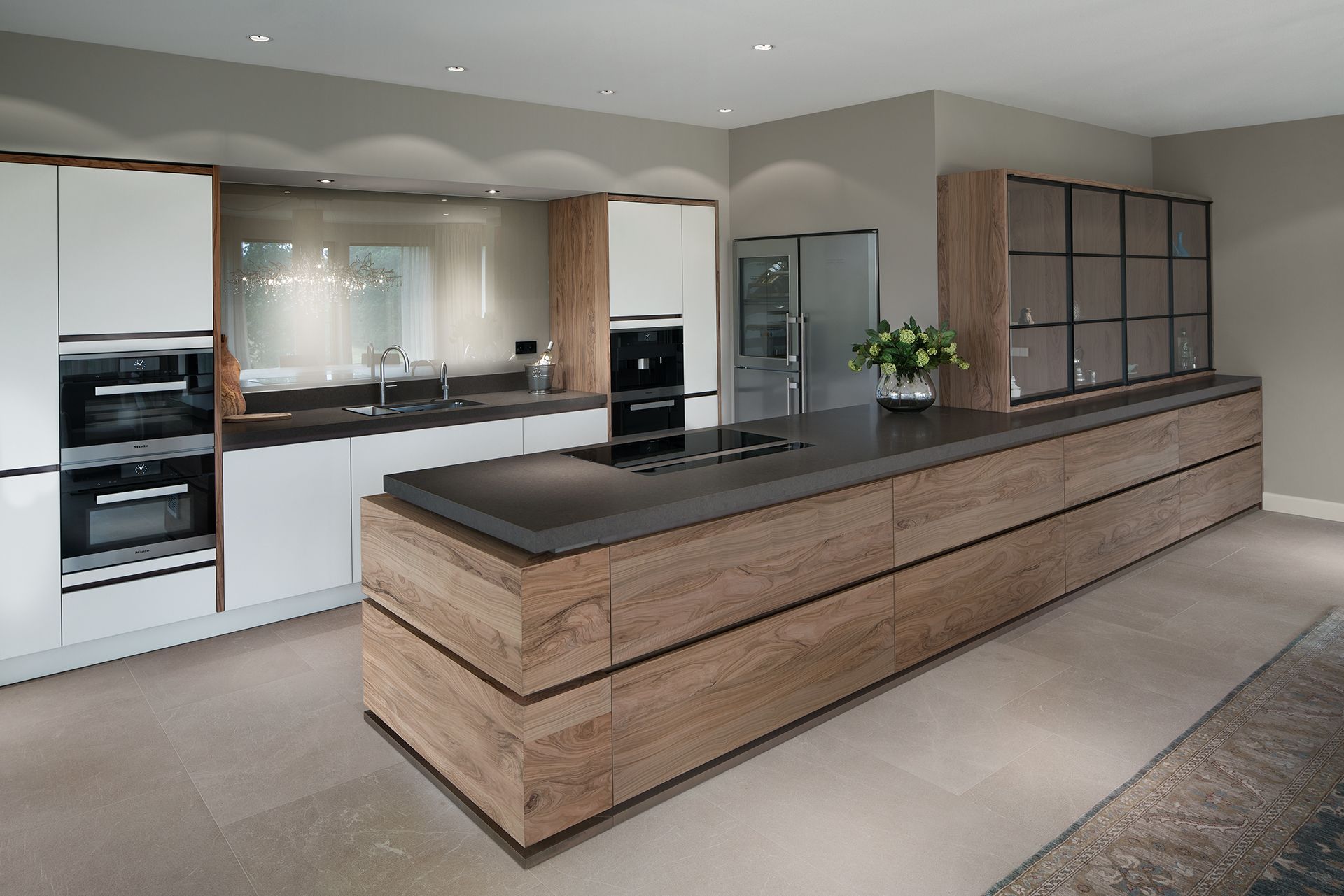 Een moderne keuken komt tot leven door de combinatie van strak witte fronten en levendig olijfhout. Verborgen blikvanger is de