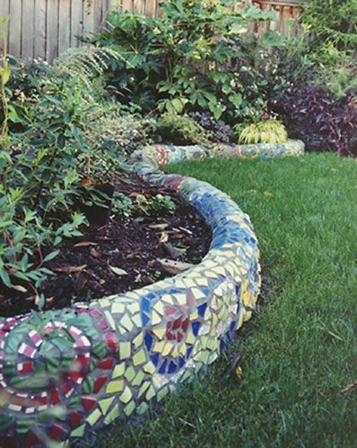 Colorful glass and tile are cut and combined into a swirling mosaic on this small curving wall set off by plants that accent the