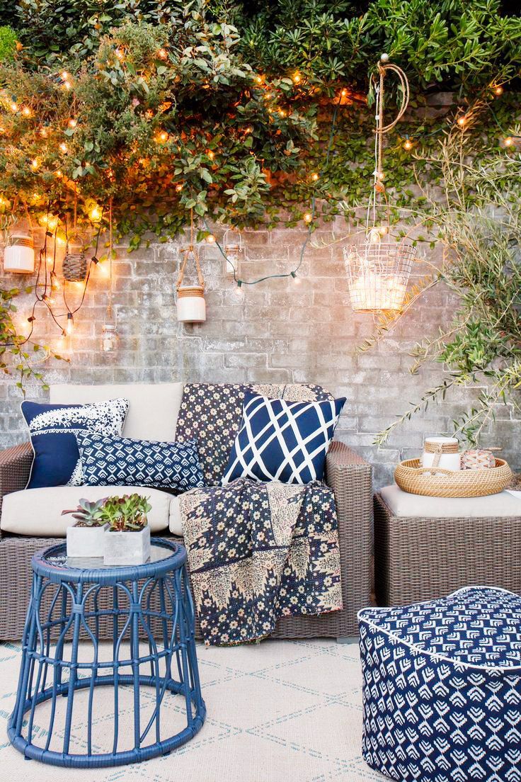 Stone outdoor space with blue pillows, neutral sofa, and hanging lights