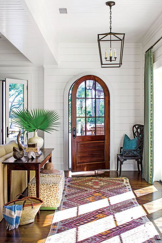 Island-style infused entryway with an iron pendant lantern, palm frond arrangement and vintage Indian runner rug.