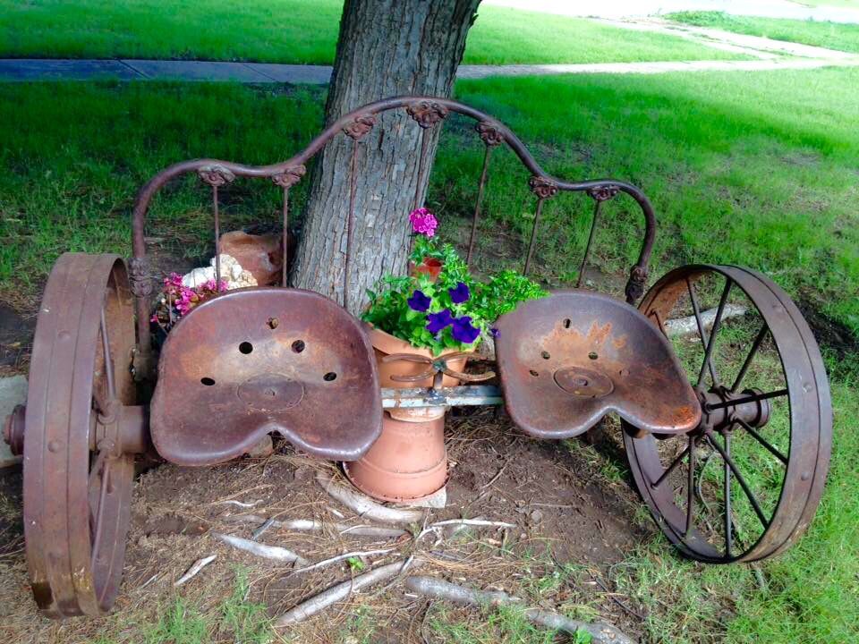 Old iron headboard, wheels and tractor seats repurposed into a bench. Horse shoes serve as drink holders.