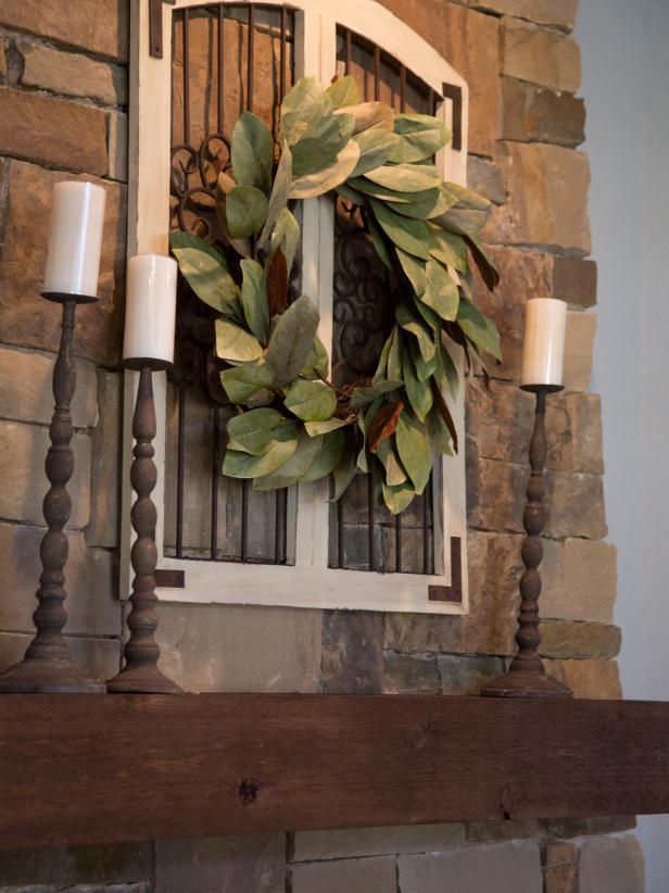 Living Room decor – rustic farmhouse style. Fireplace mantel scape featuring a magnolia wreath over a window frame with tall